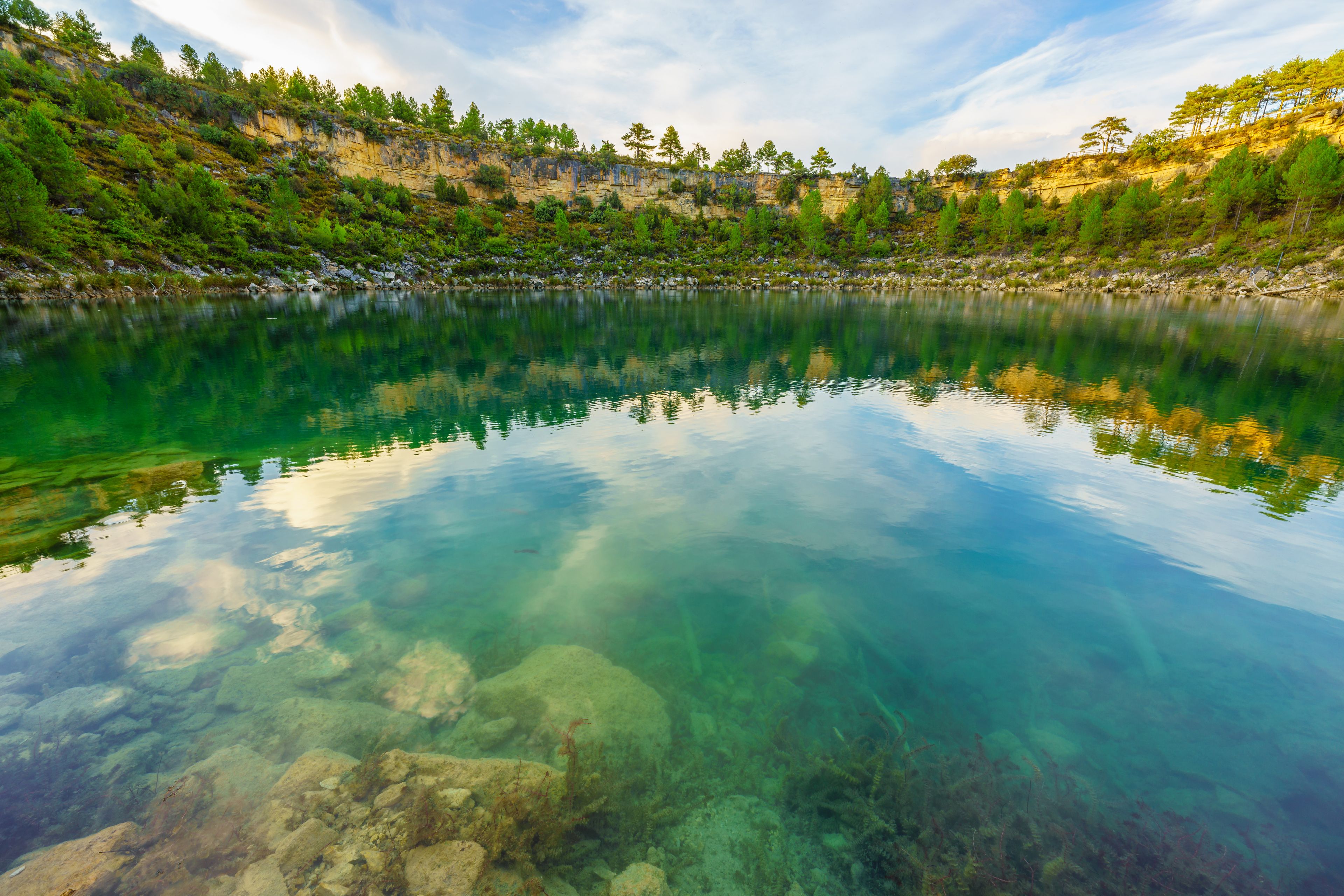 Ein klarer See mit Spiegelungen der umliegenden Bäume und des Himmels.