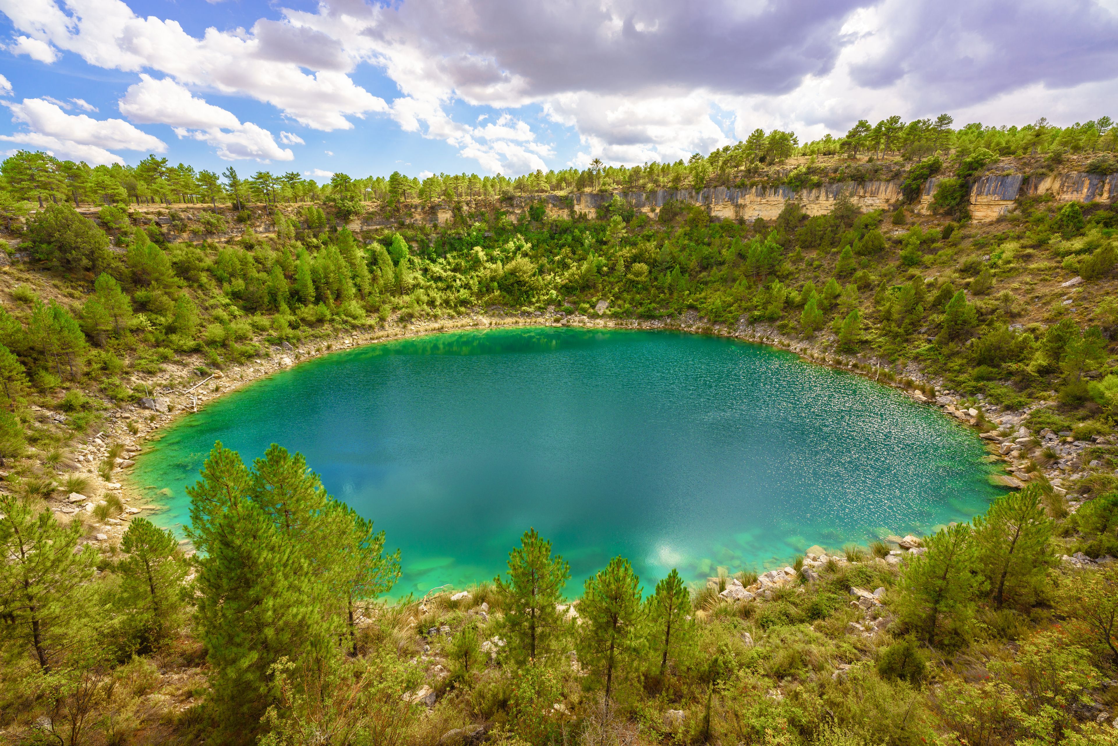 Ein türkisfarbener See, umgeben von dichtem, grünen Wald und steinigen Klippen.
