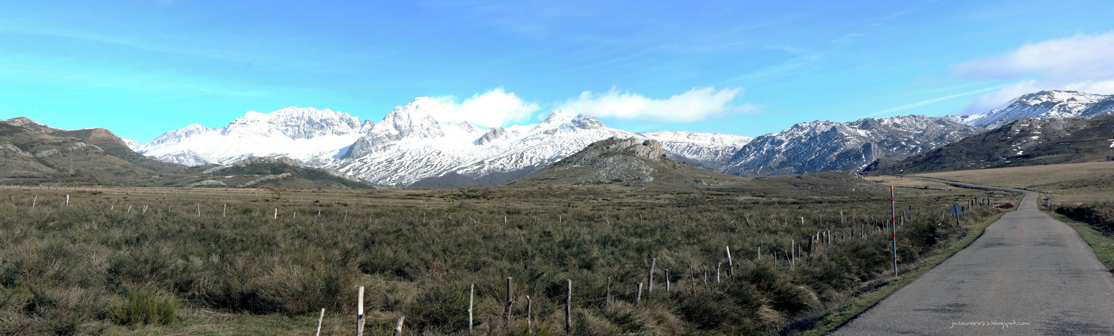 A road leading through a mountainous landscape with snow-capped peaks in the background.