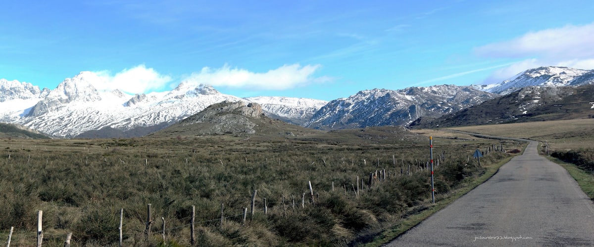 A road leading through a mountainous landscape with snow-capped peaks in the background.