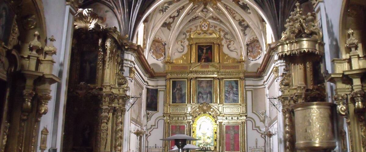An ornate church interior with a high vaulted ceiling, golden altars, and religious paintings.