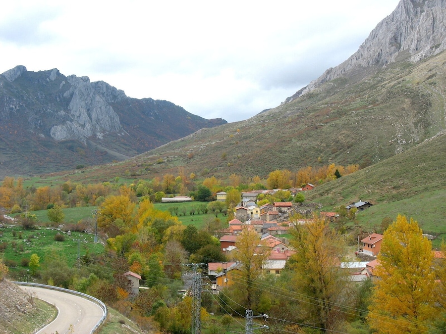 A village nestled in a valley with autumn-colored trees, surrounded by mountains.