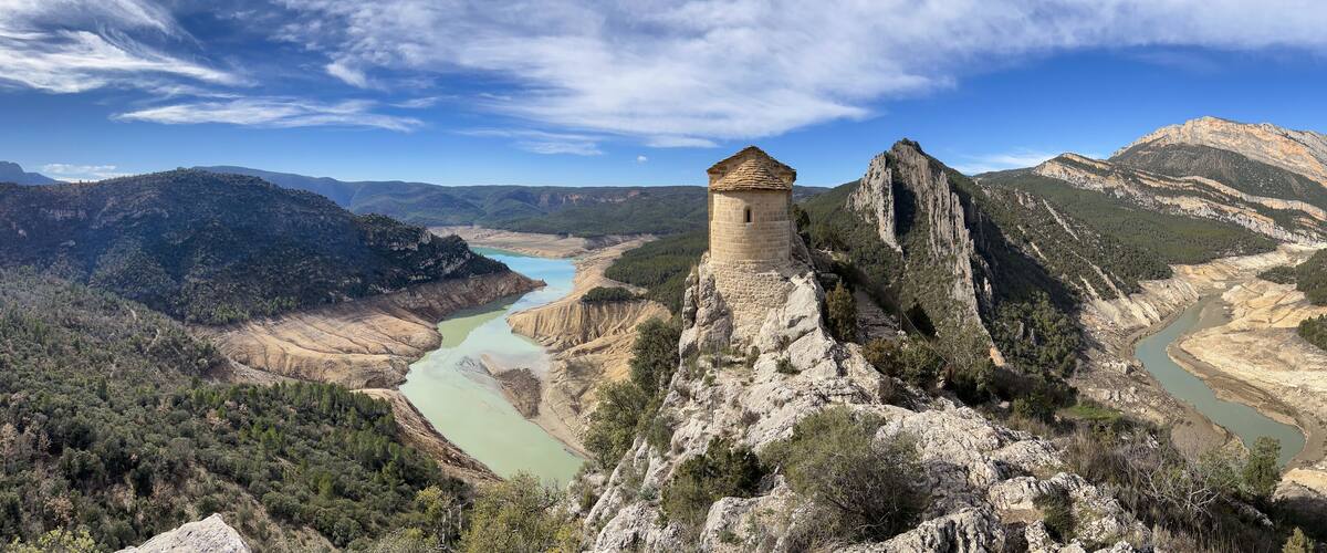 A stone tower on a cliff overlooking a river valley with mountains in the background.