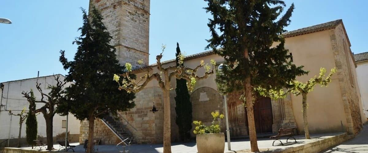 A historic church with a bell tower, surrounded by trees and a paved courtyard.