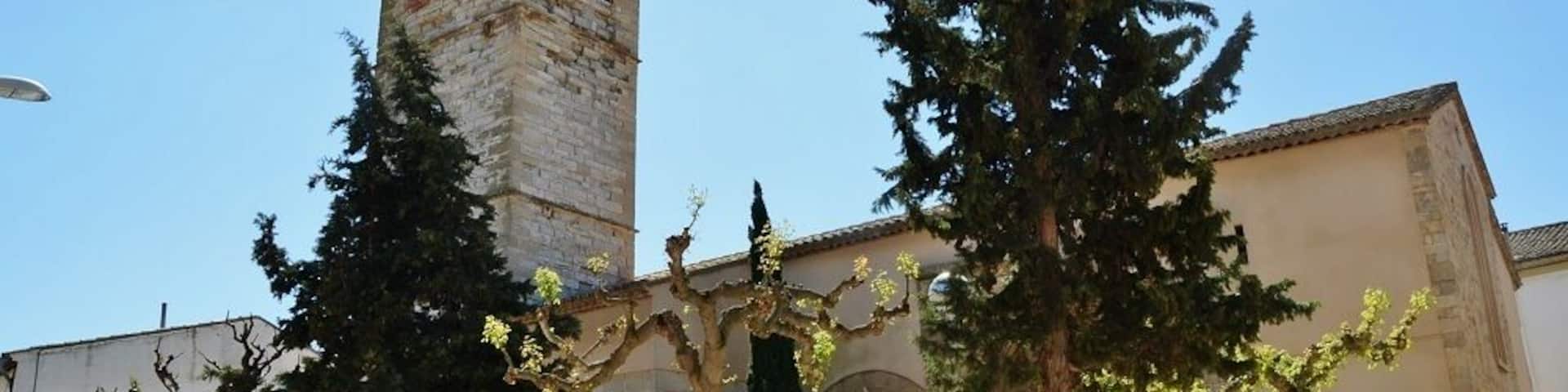 A historic church with a bell tower, surrounded by trees and a paved courtyard.