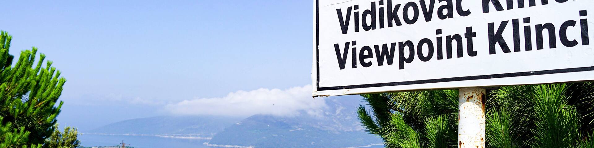 Viewpoint in the village of Klinci on the Lustica peninsula: a sign with the name of the location and a view of the Bay of Kotor in the background. Summer landscape from the coast of Montenegro