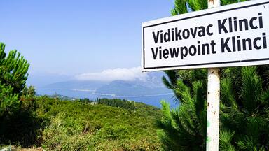 Viewpoint in the village of Klinci on the Lustica peninsula: a sign with the name of the location and a view of the Bay of Kotor in the background. Summer landscape from the coast of Montenegro