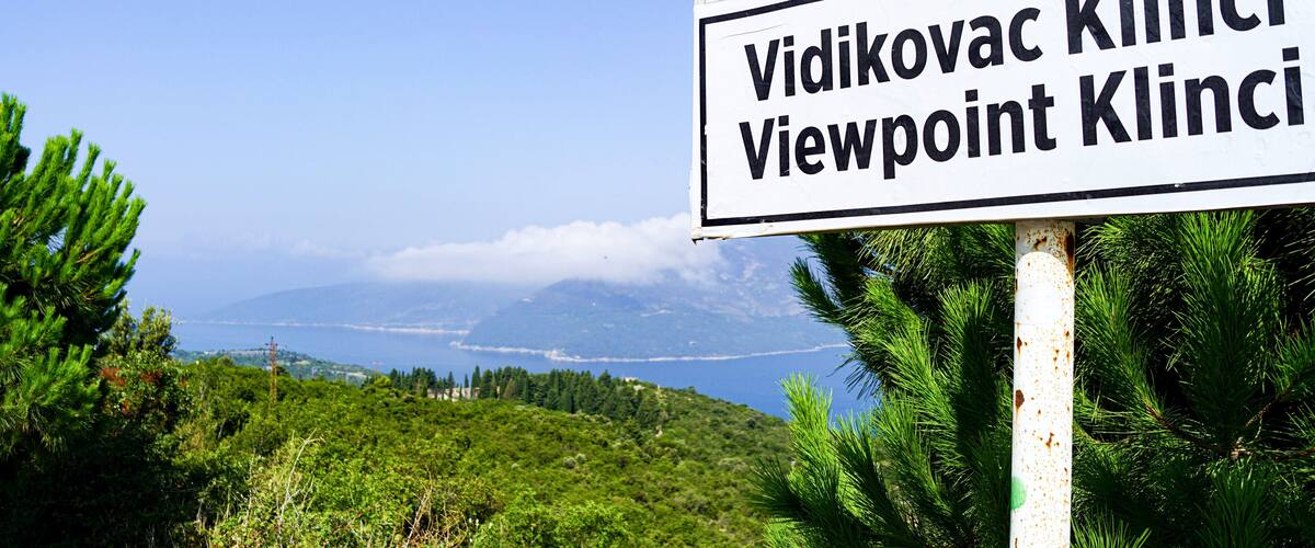 A sign with 'Vidikovac Klinci Viewpoint Klinci' text, surrounded by greenery and a scenic view of a coastline.