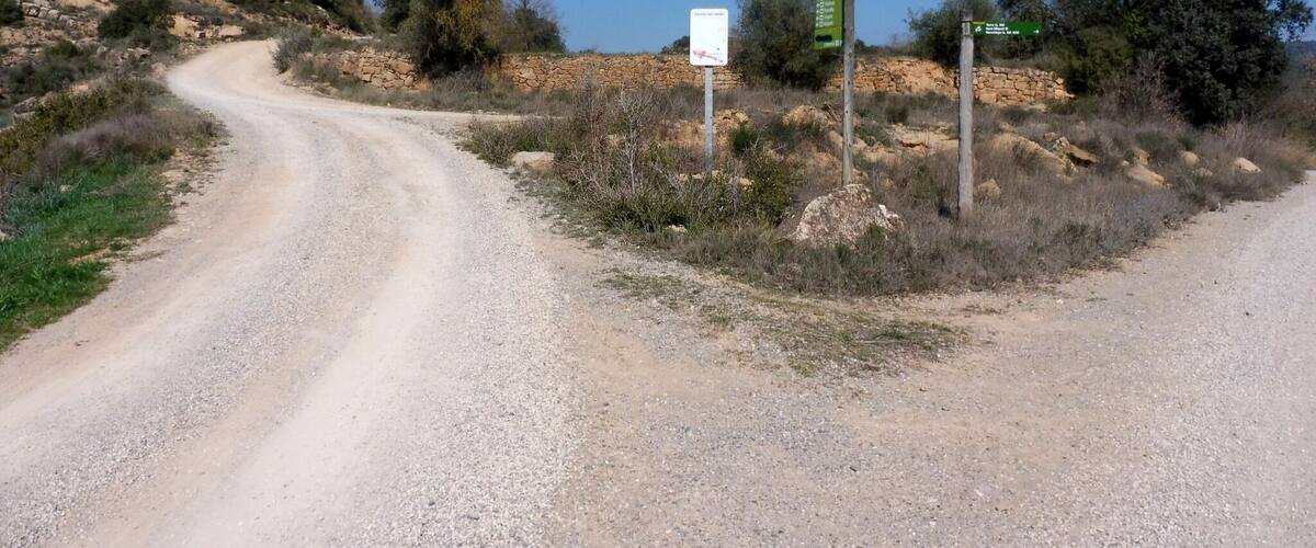 A gravel road winding through a dry, hilly landscape with sparse vegetation and a clear blue sky.
