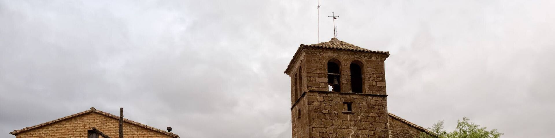 A historic stone building with a bell tower, surrounded by gravel and greenery.