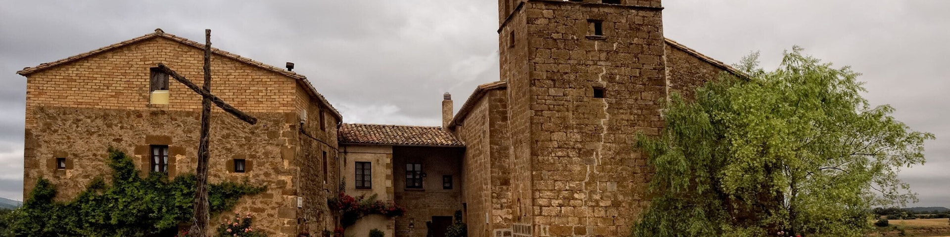 Um edifício histórico de pedra com um campanário, rodeado por cascalho e vegetação.