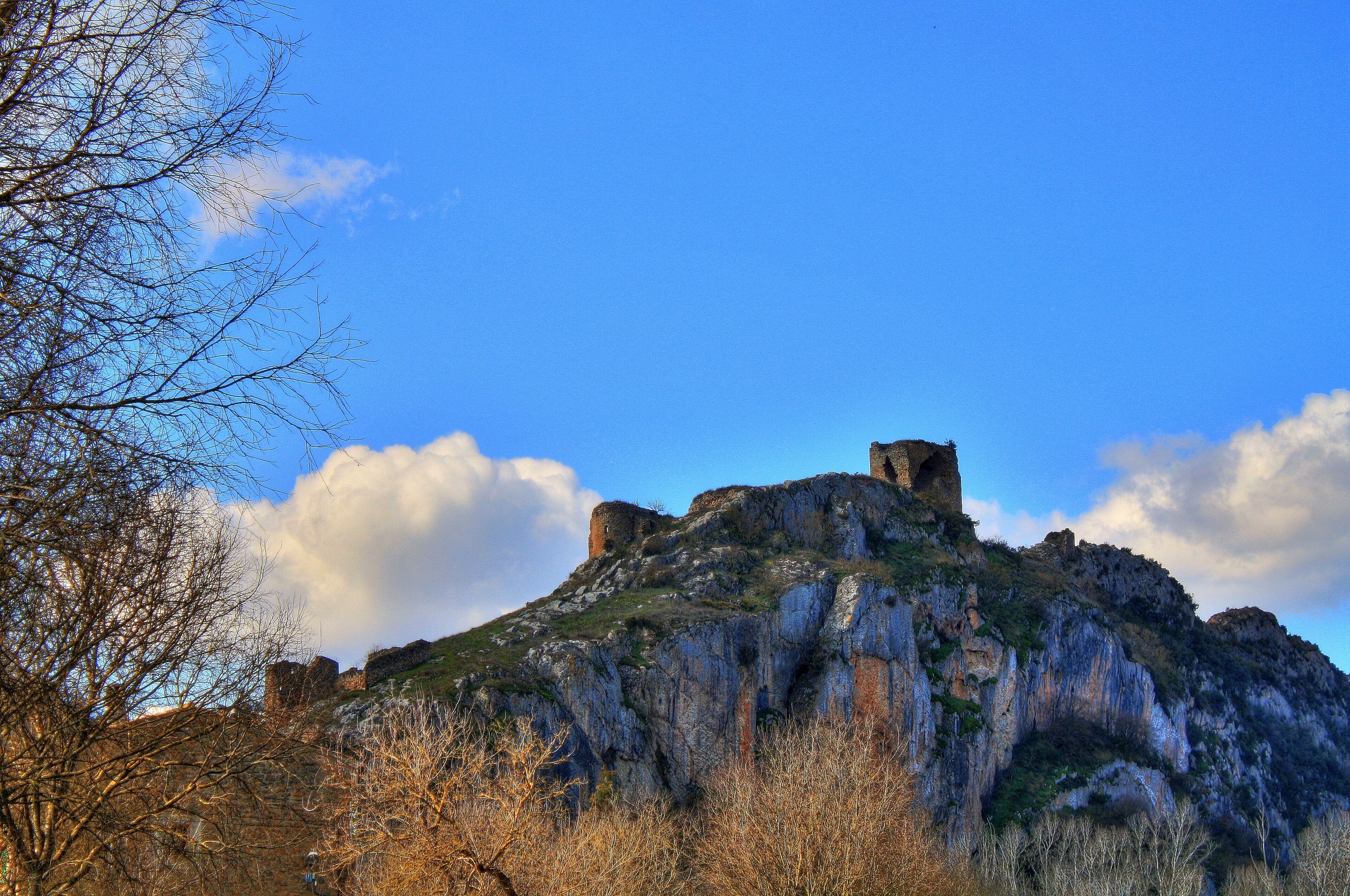 A rocky hill with a castle ruin and sparse vegetation.
