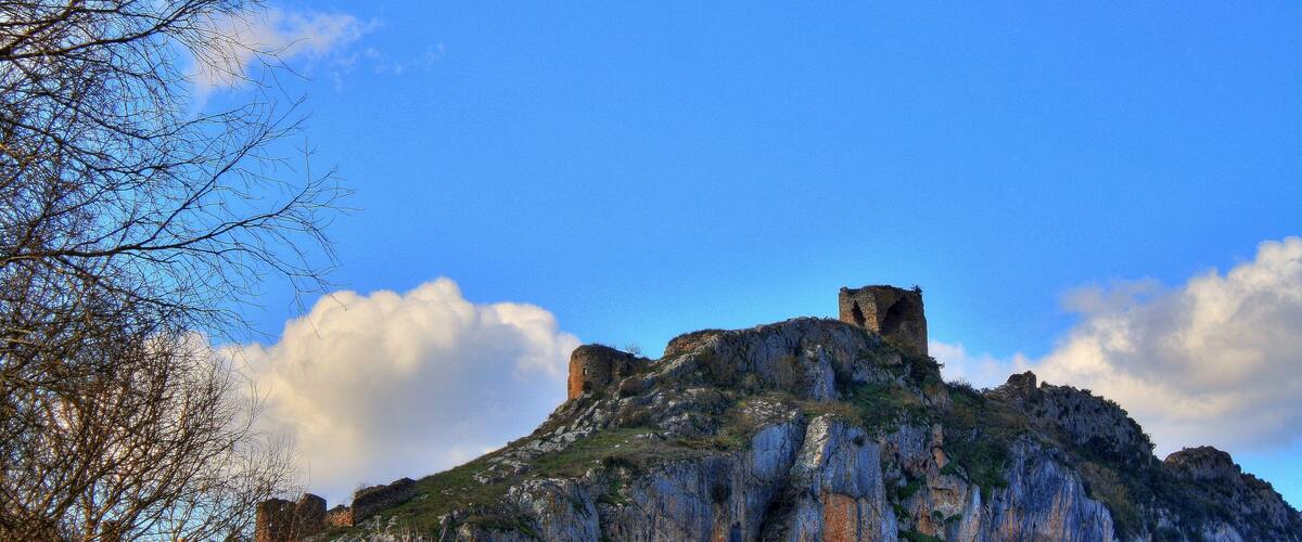 A rocky hill with a castle ruin and sparse vegetation.