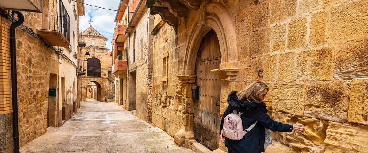 Tourist woman touching the medieval stone of the historic buildings of the town of Cretas, Teruel, Aragon.