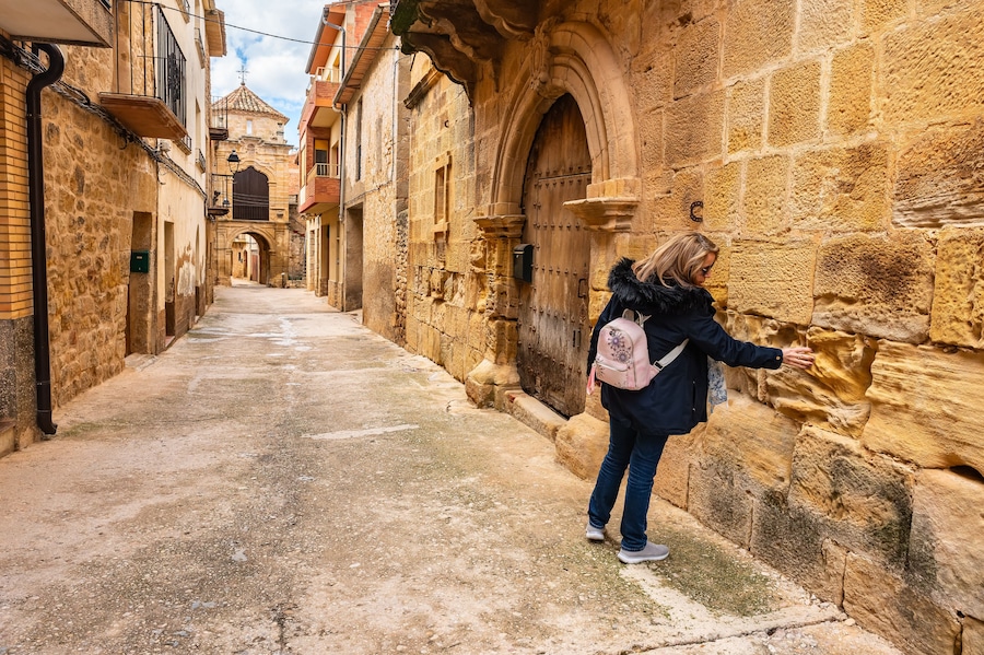 Tourist woman touching the medieval stone of the historic buildings of the town of Cretas, Teruel, Aragon.