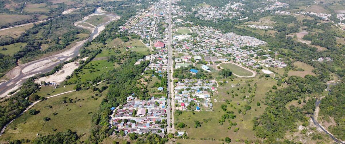 An aerial view of a town with a river running through it, surrounded by green hills and mountains.