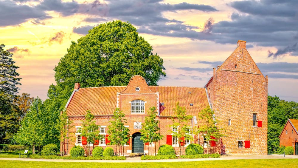 A brick building with a tower, surrounded by trees and a grassy field.