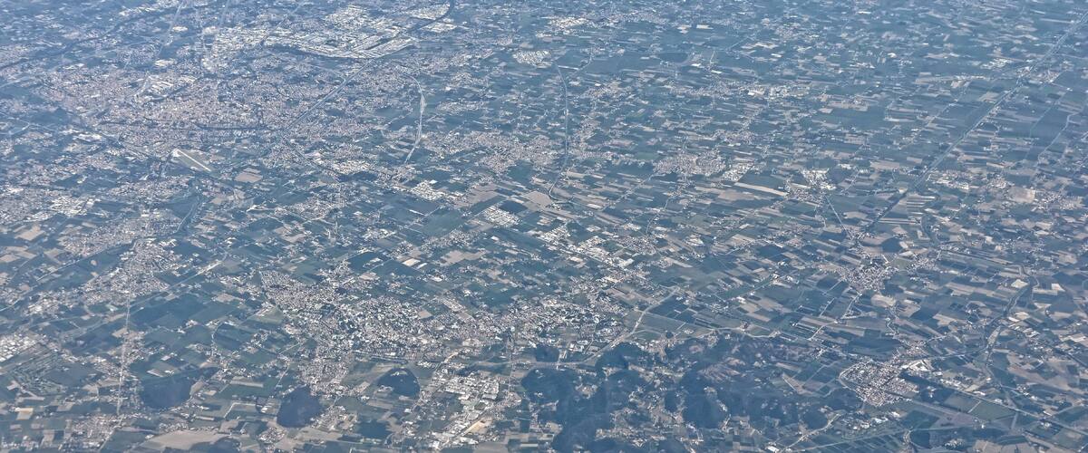 An aerial view of a densely populated urban area with a mix of residential and commercial buildings, roads, and patches of green spaces.