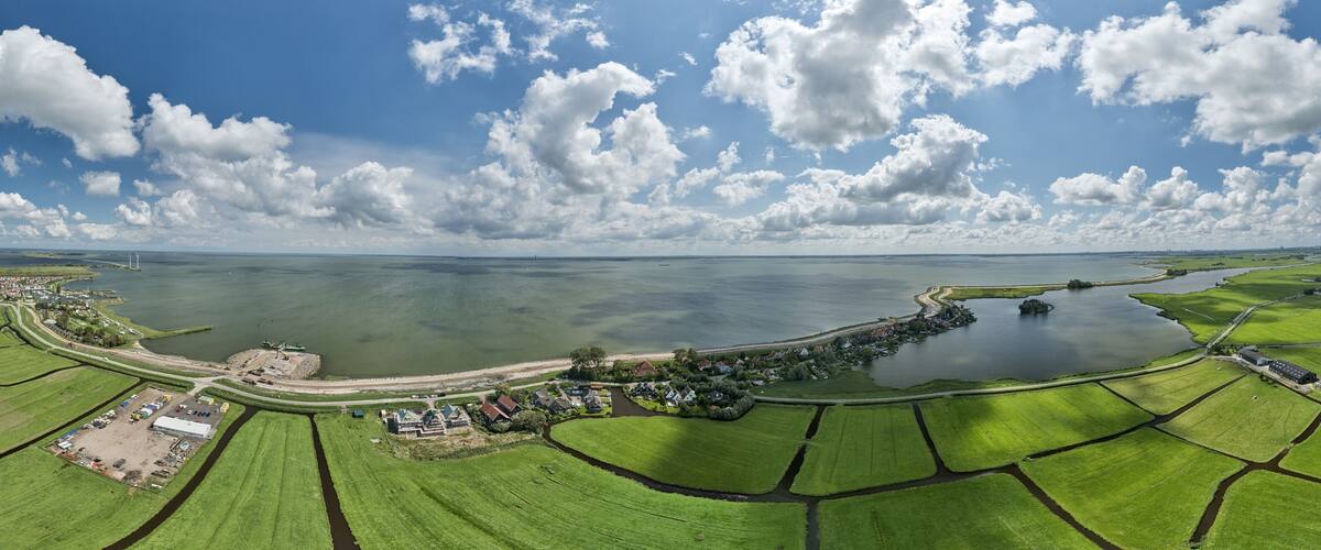 An aerial view of a coastal landscape with green fields, a body of water, and a small settlement with houses and a large building.