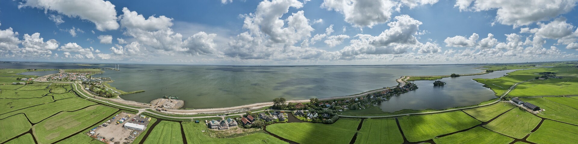 An aerial view of a coastal landscape with green fields, a body of water, and a small settlement with houses and a large building.