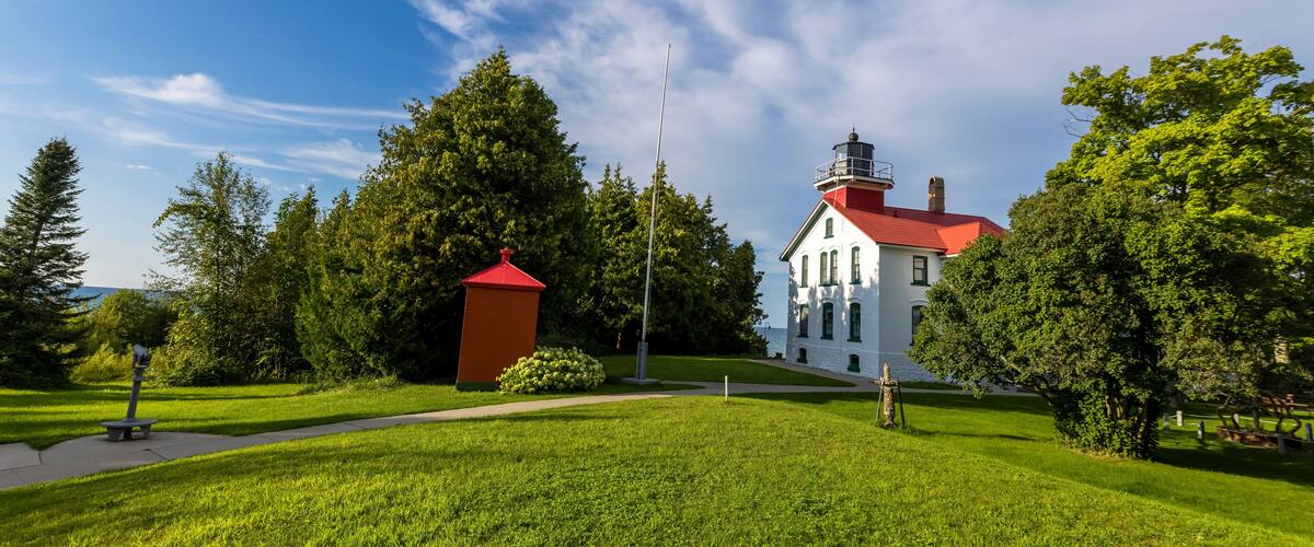 A white building with a red roof, surrounded by green grass and trees.