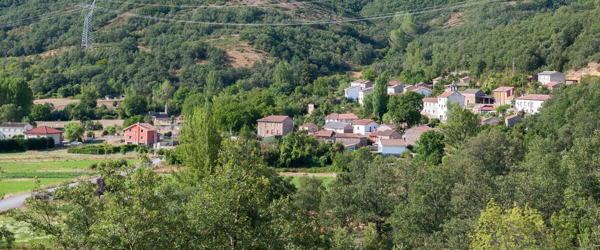 A village nestled in a valley with a backdrop of lush green hills and a power line running across the landscape.