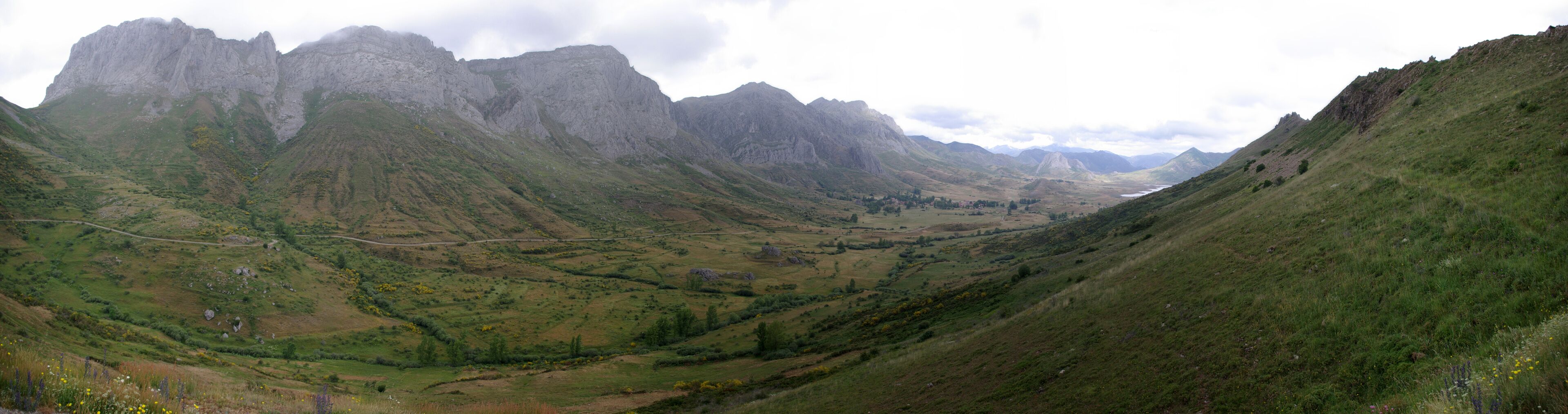 A valley with a winding road, green hills, and rocky mountains.