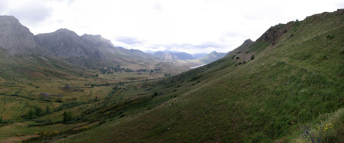 A valley with a winding road, green hills, and rocky mountains.