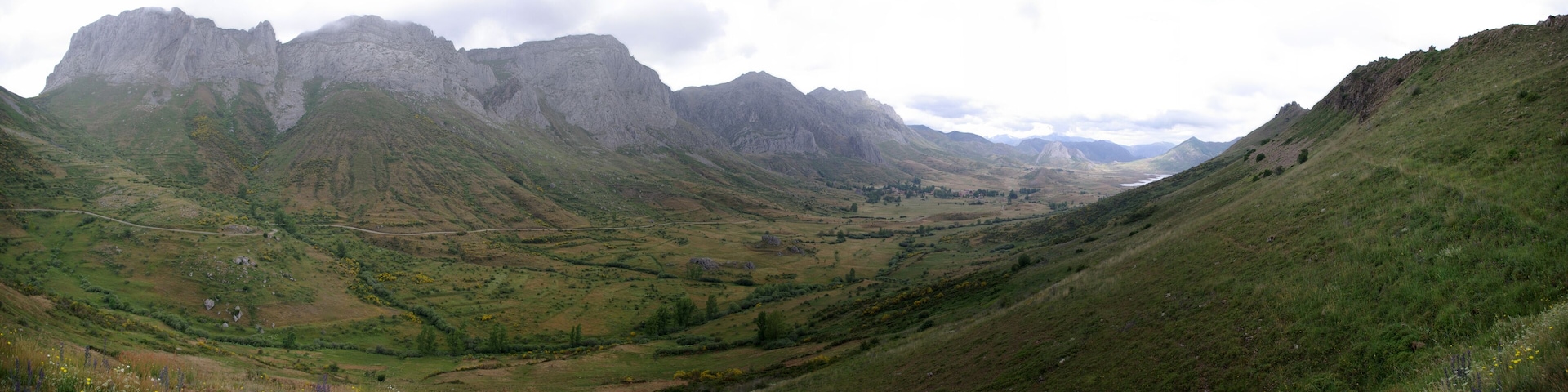 A valley with a winding road, green hills, and rocky mountains.