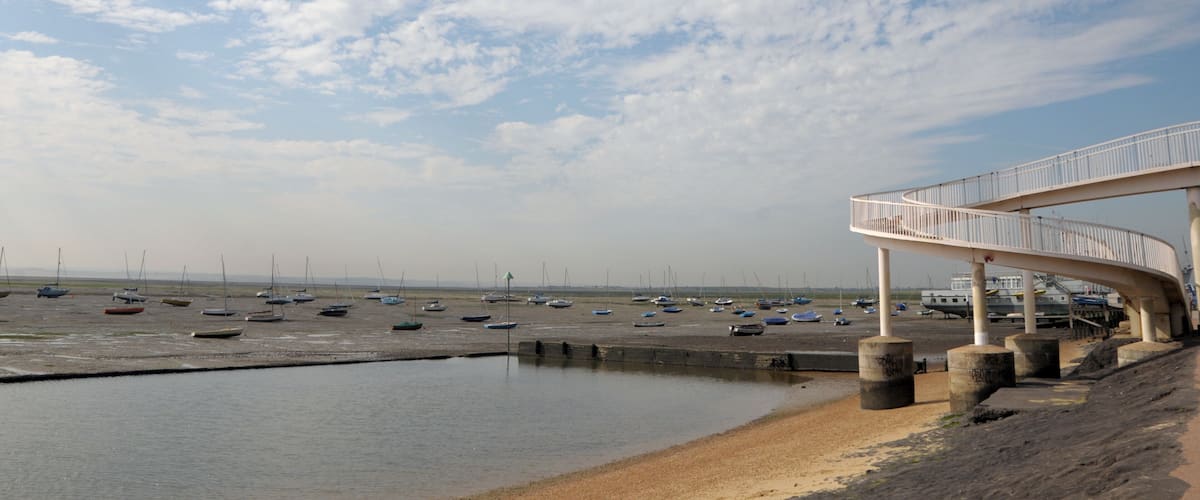 A beach with boats, a curved walkway, and a cloudy sky.