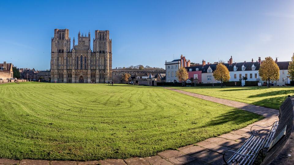 A cathedral with twin towers, a well-maintained lawn, and traditional buildings in the background.