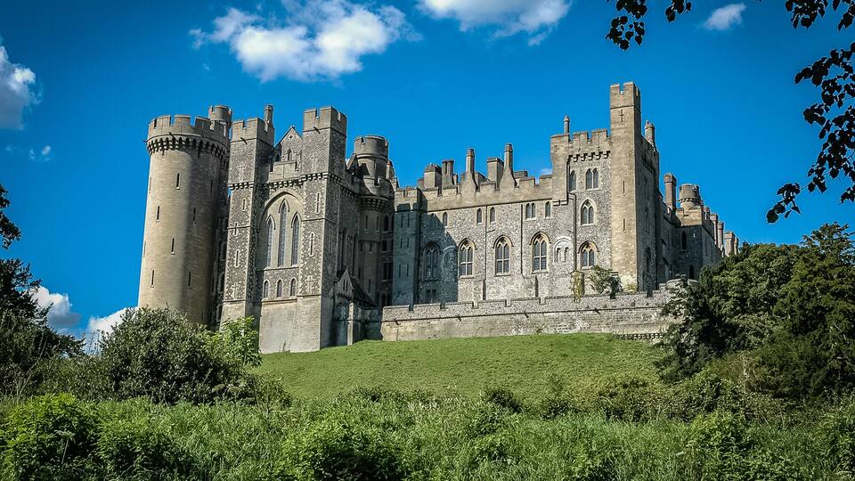 A large medieval castle with multiple towers and a grassy hill in the foreground.