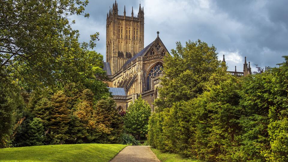 A cathedral with a tall tower, surrounded by lush greenery and a pathway leading to it.