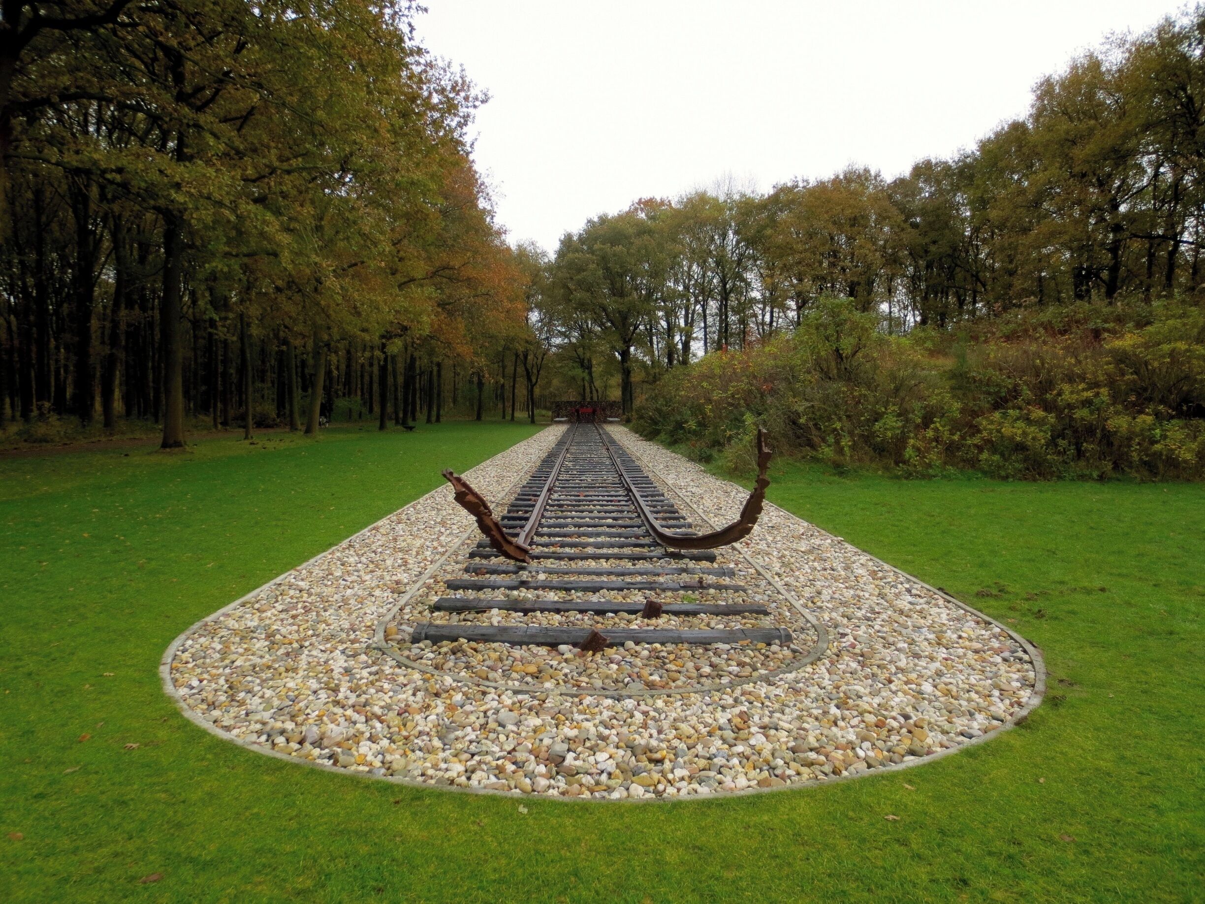 A railway track in a park surrounded by trees and pebbles.