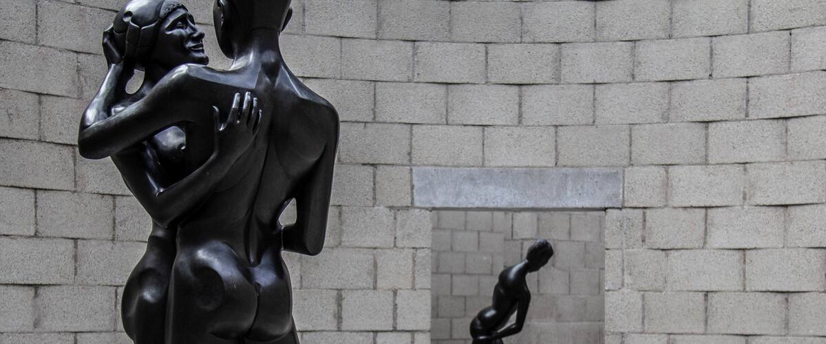 A sculpture of a couple in an intimate pose, set against a backdrop of a brick wall.