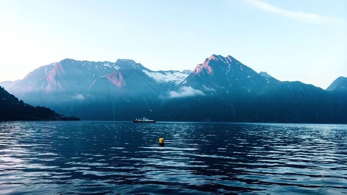 A calm lake with a boat and a buoy, surrounded by snow-capped mountains.