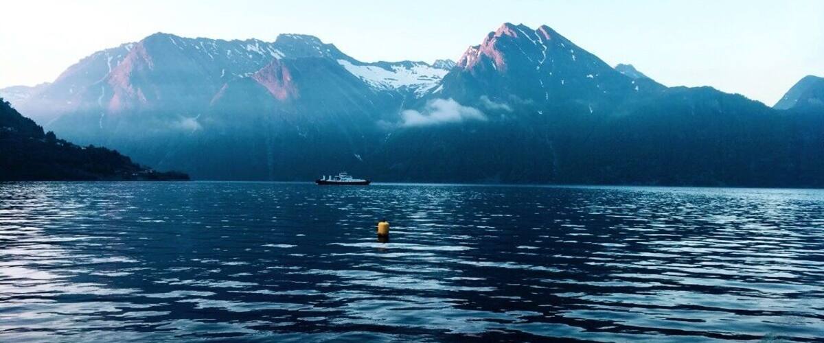 A calm lake with a boat and a buoy, surrounded by snow-capped mountains.