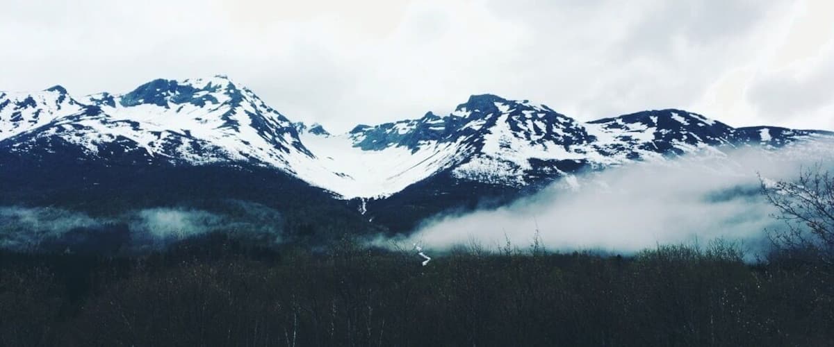 Snow-capped mountains, a forested valley, and a misty atmosphere.