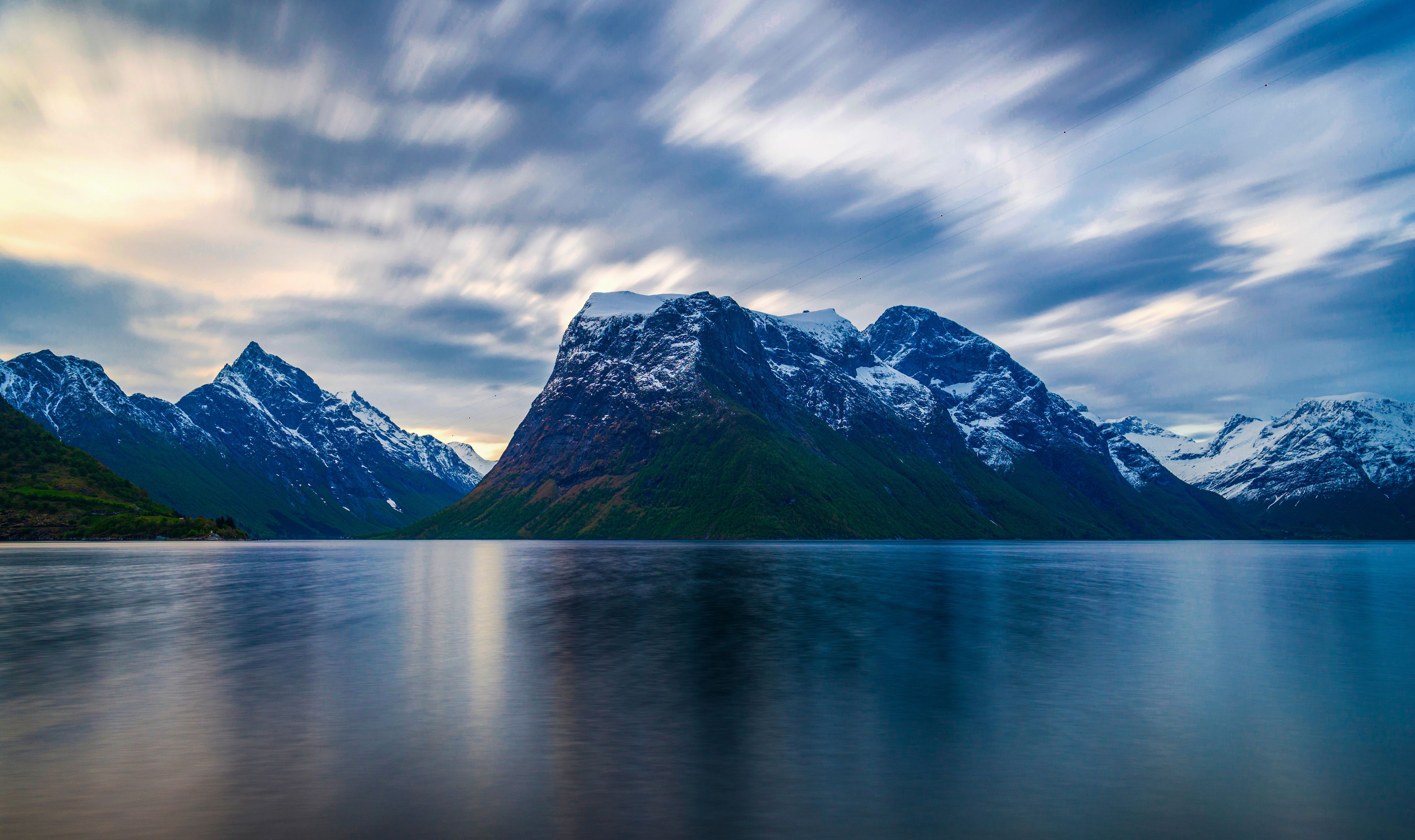 A mountain range with snow-capped peaks and a calm lake in the foreground.
