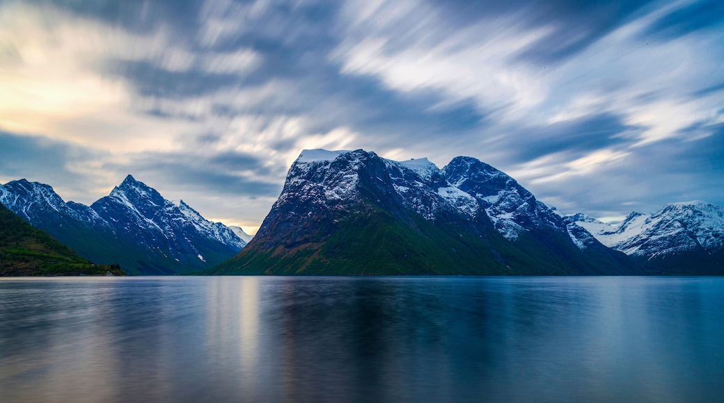 A mountain range with snow-capped peaks and a calm lake in the foreground.