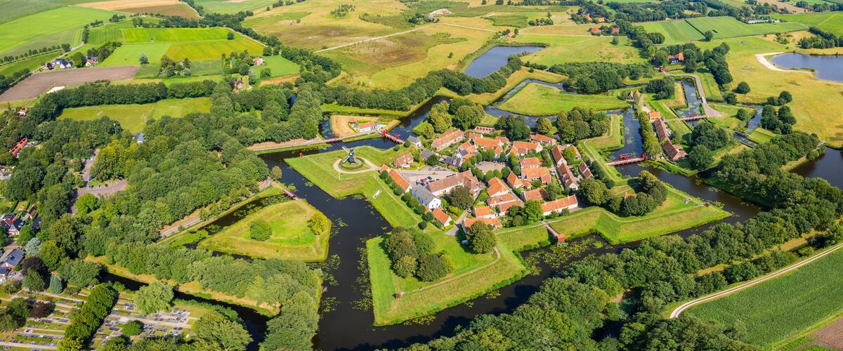 An aerial view of a historic town with a moat, surrounded by fields and a river.