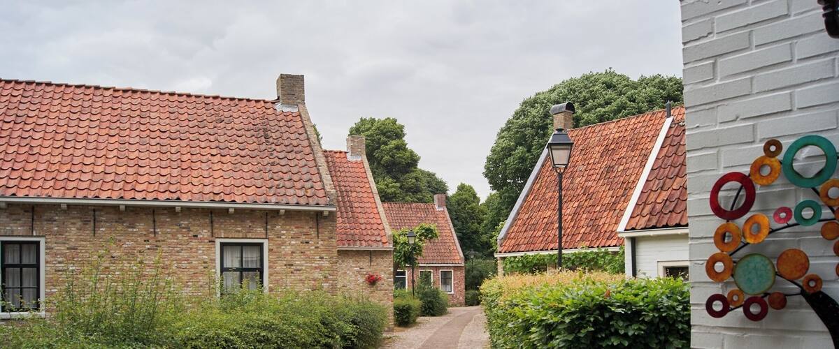 A narrow cobblestone street flanked by traditional brick houses with red-tiled roofs, surrounded by lush greenery.