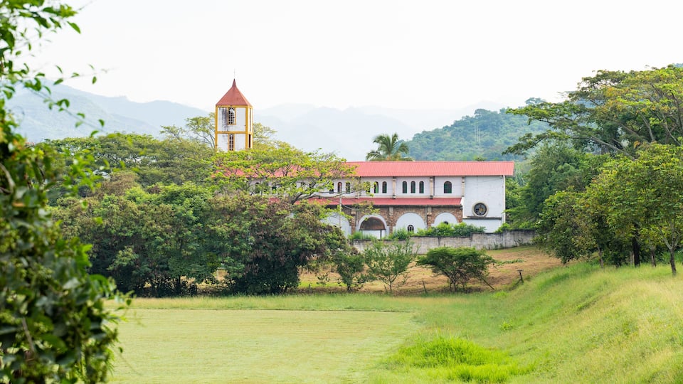 A church with a bell tower, surrounded by lush greenery and hills in the background.