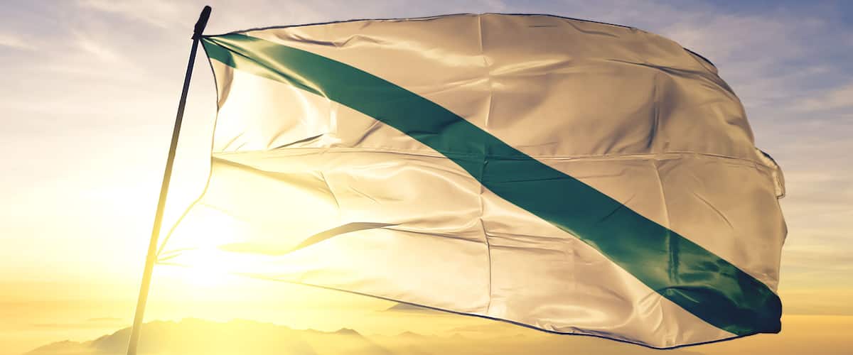 A flag waving against a sunrise with mountains in the background.