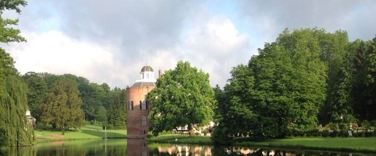 A serene pond with a tower and a dome structure in the background, surrounded by lush greenery.