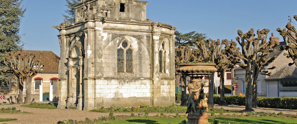 Un bâtiment historique en pierre, doté d’un dôme, de fenêtres en arc de cercle et d’une statue dans un jardin.
