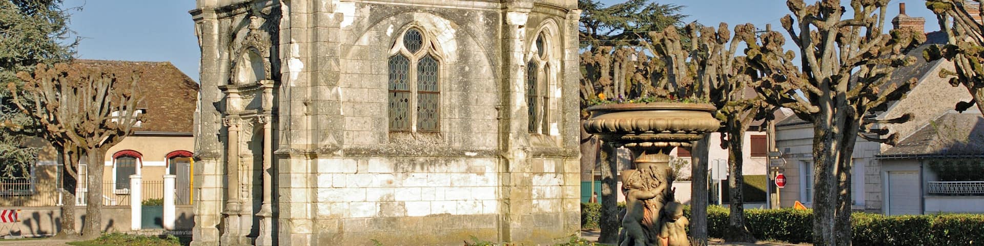 A historic stone building with a dome, arched windows, and a statue in a garden.