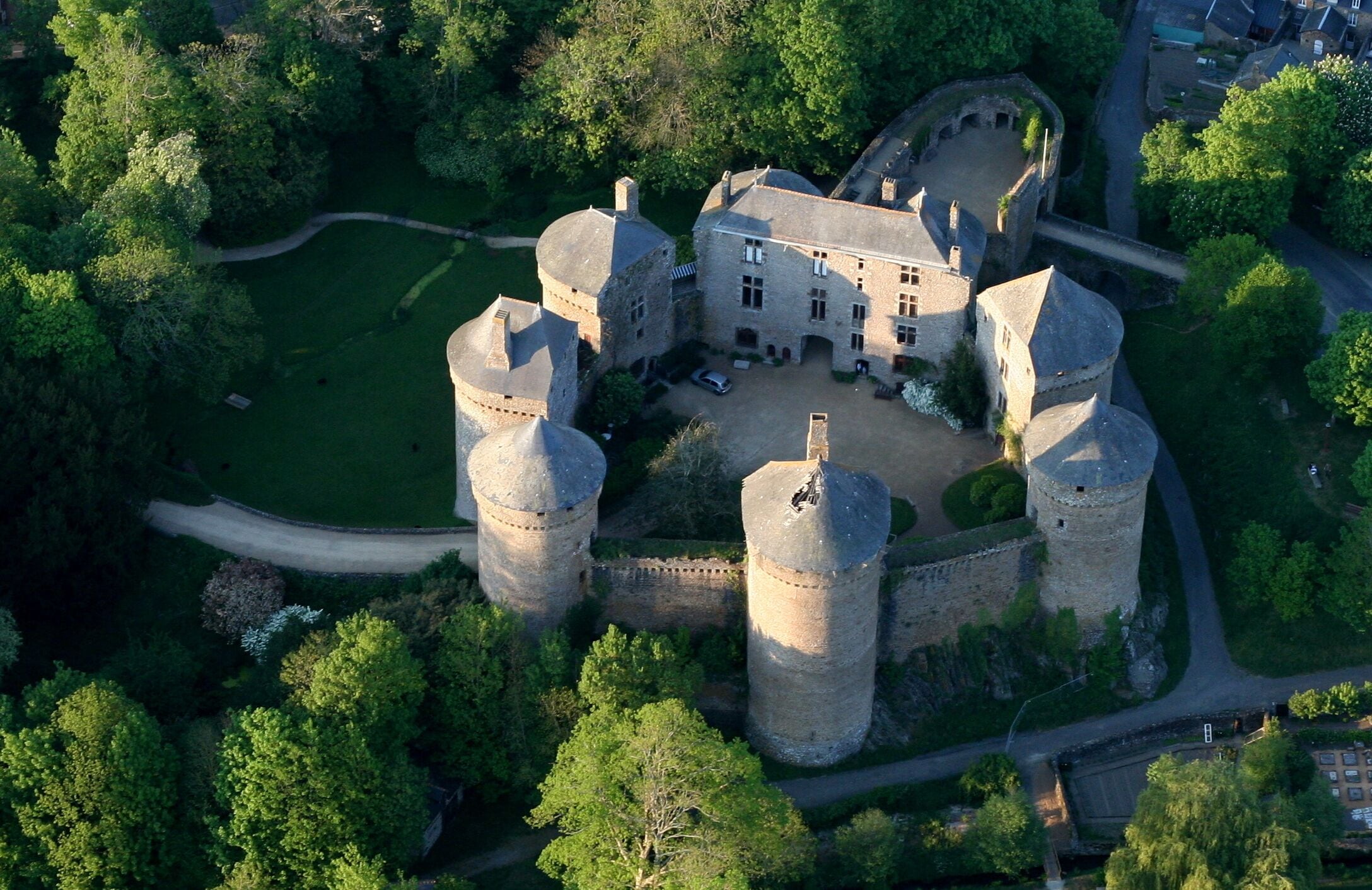 Vista aérea de un castillo rodeado de abundante vegetación y un foso.