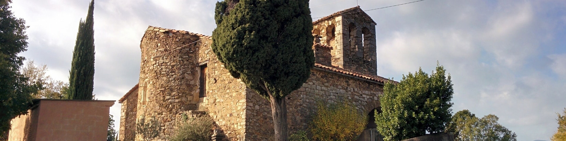 Un antiguo edificio de piedra con un campanario, rodeado de árboles y un campo cubierto de hierba.