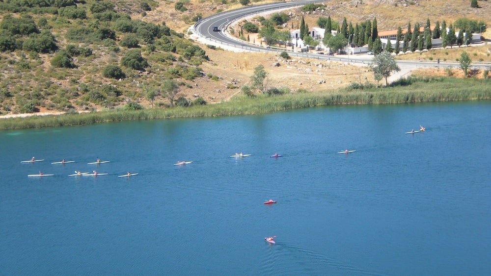 A lake with several boats, a winding road, and a hilly landscape with sparse vegetation.